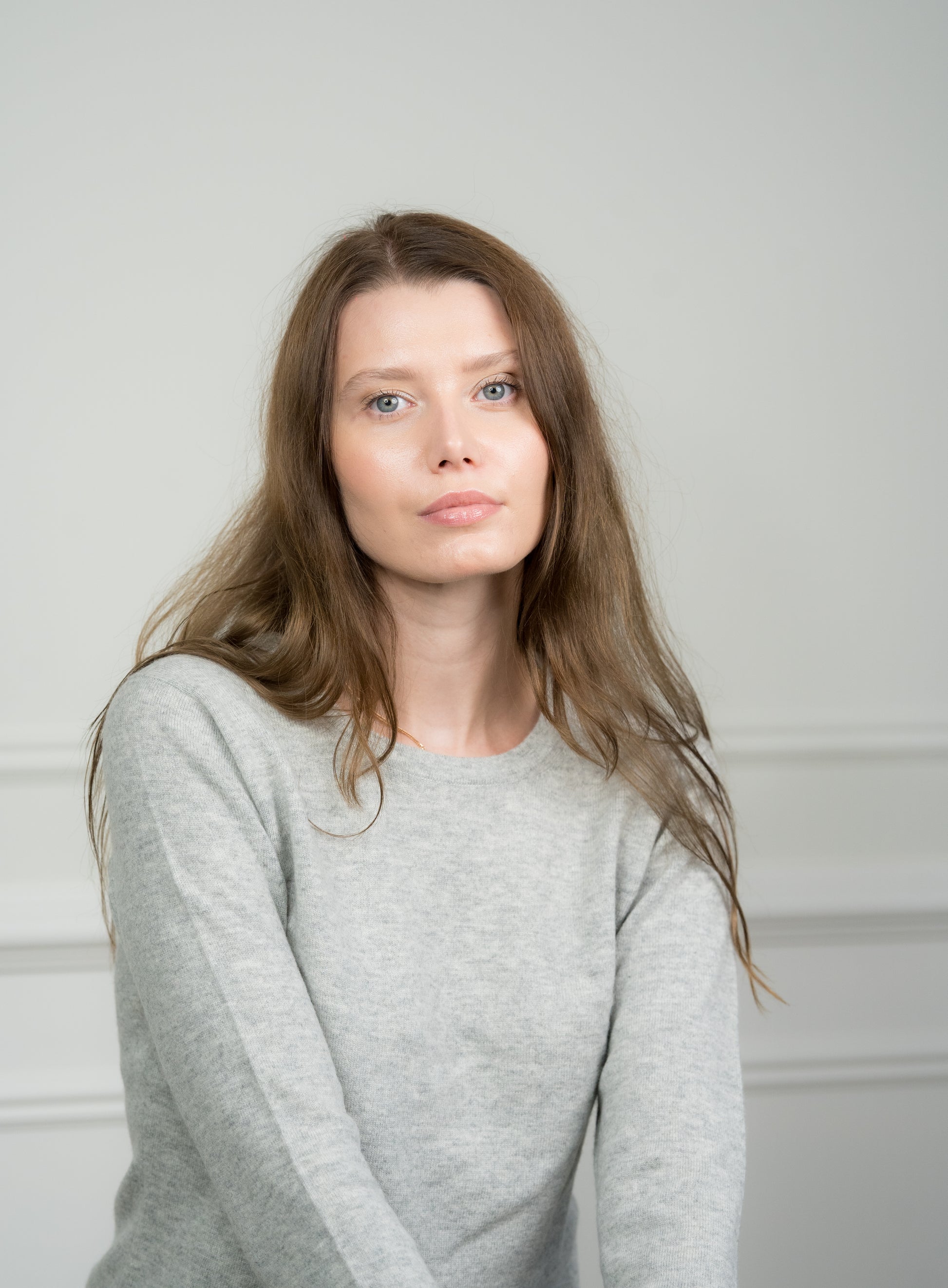 Side view of the light grey crew neck jumper worn by a model, emphasizing its tailored fit and ribbed cuffs.